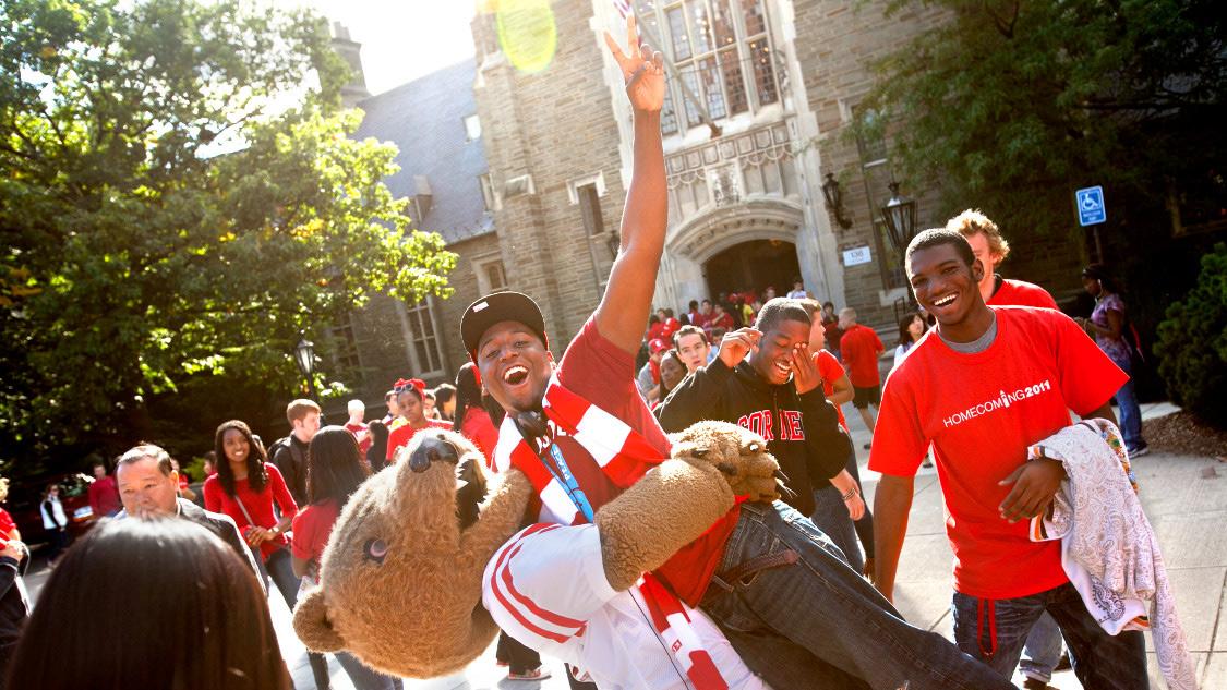 Cornell Bear hoists student up who is making a peace sign with his hand